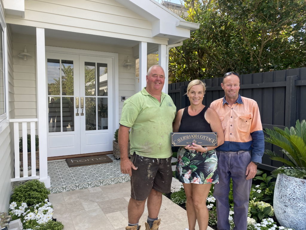 Doug the builder “hands over” Caversham Cottage to proud owners, Christine and Anthony. Christine holds the sign with the name of the house and the year it was constructed.