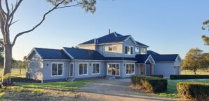 The Eternal Flame is a double storey weather board home located on a horse adjustment property. The weatherboards are grey, the Standing Seam roofing is black, and the windows, architraves and trims to the house are white.